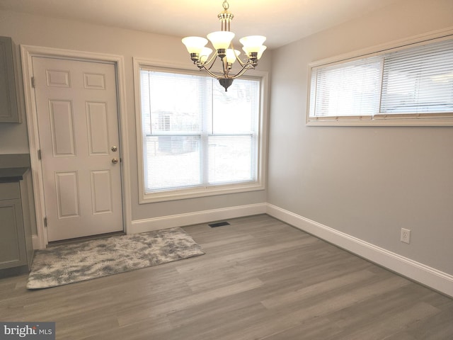 unfurnished dining area with a chandelier, wood finished floors, visible vents, and baseboards