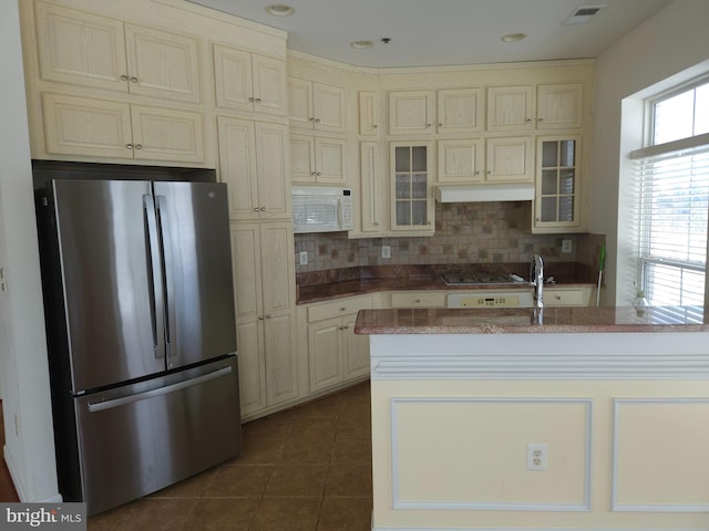 kitchen featuring stainless steel refrigerator, backsplash, cream cabinets, and dark tile patterned floors