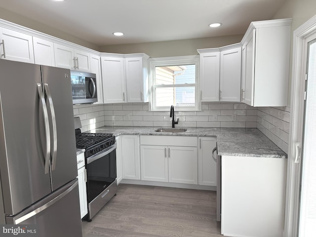 kitchen with sink, appliances with stainless steel finishes, light stone counters, light hardwood / wood-style floors, and white cabinets