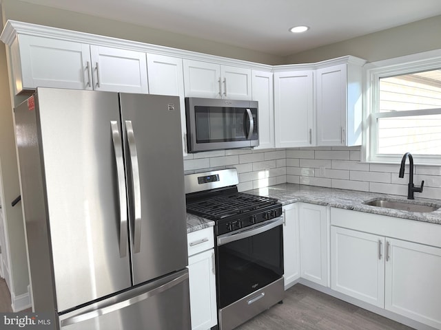 kitchen with white cabinetry, sink, light stone counters, and appliances with stainless steel finishes