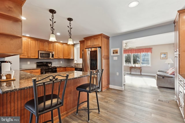 kitchen with sink, dark stone countertops, black appliances, a kitchen bar, and decorative light fixtures