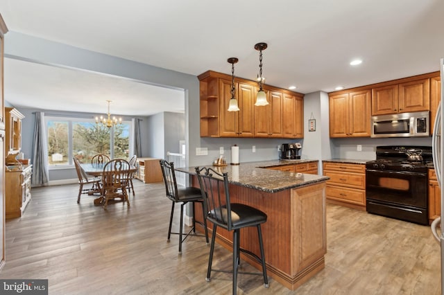 kitchen featuring a breakfast bar, pendant lighting, dark stone countertops, black range with gas stovetop, and kitchen peninsula