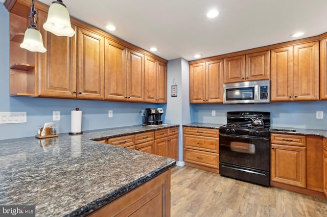 kitchen featuring black range with gas stovetop, dark stone counters, hanging light fixtures, and light wood-type flooring