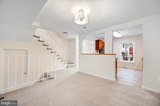 spare room with stairs, baseboards, visible vents, and light colored carpet