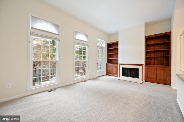 unfurnished living room with baseboards, visible vents, a fireplace with raised hearth, and light colored carpet