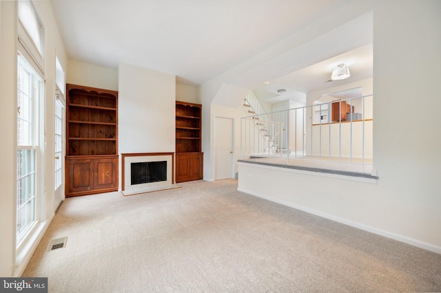 unfurnished living room with visible vents, a fireplace with raised hearth, stairway, light carpet, and baseboards