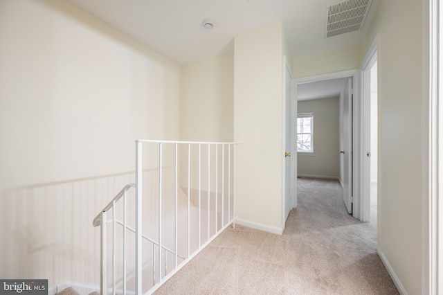 hallway with light carpet, baseboards, visible vents, and an upstairs landing