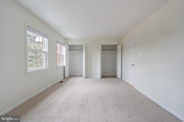 unfurnished bedroom featuring baseboards, two closets, visible vents, and light colored carpet