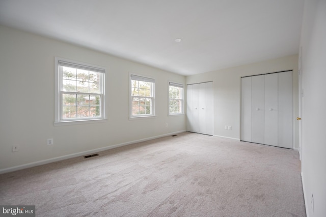 unfurnished bedroom with baseboards, two closets, visible vents, and light colored carpet