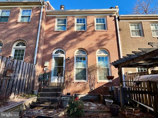 view of property featuring brick siding, fence, and central AC