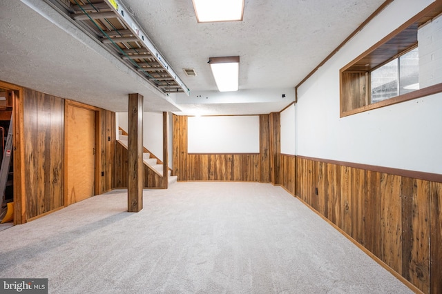 below grade area featuring wooden walls, visible vents, wainscoting, stairs, and a textured ceiling