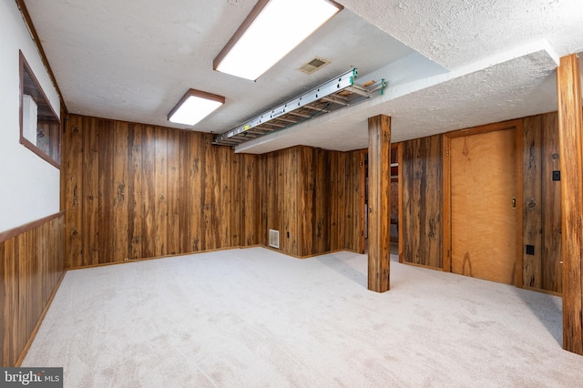 finished below grade area with light carpet, wood walls, a textured ceiling, and visible vents