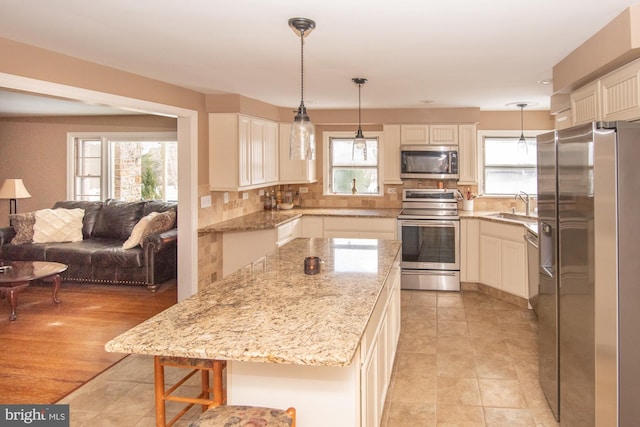 kitchen featuring decorative light fixtures, tasteful backsplash, sink, stainless steel appliances, and light stone countertops