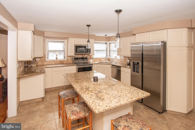 kitchen featuring sink, appliances with stainless steel finishes, hanging light fixtures, a center island, and a kitchen bar