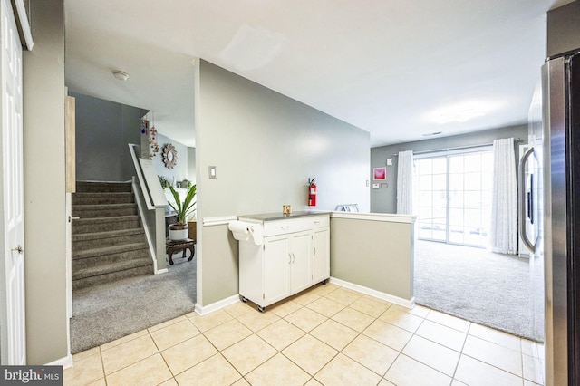 kitchen featuring light carpet, kitchen peninsula, stainless steel refrigerator, and white cabinets