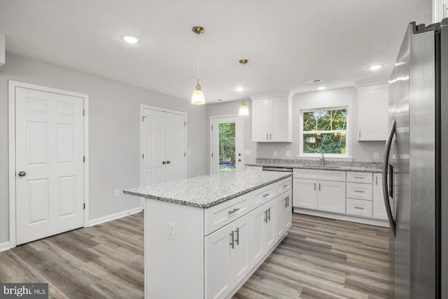 kitchen with a kitchen island, decorative light fixtures, white cabinetry, stainless steel fridge, and light stone counters