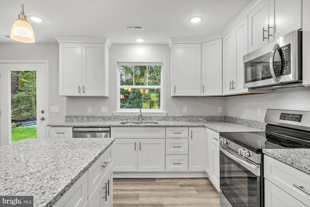 kitchen with sink, white cabinetry, hanging light fixtures, appliances with stainless steel finishes, and light stone countertops