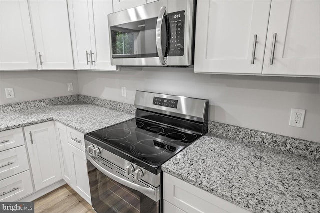 kitchen with light stone counters, appliances with stainless steel finishes, light hardwood / wood-style floors, and white cabinets