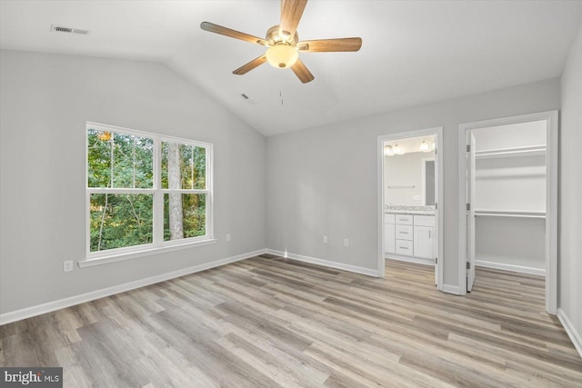 unfurnished bedroom featuring lofted ceiling, a walk in closet, light hardwood / wood-style flooring, and ensuite bath