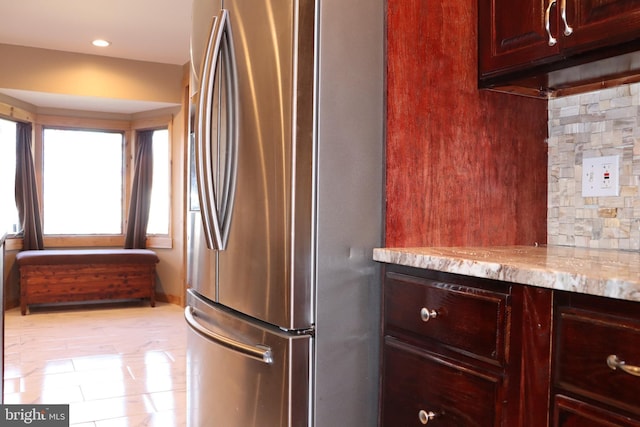 kitchen featuring light stone countertops, light tile patterned floors, stainless steel fridge, and backsplash