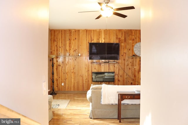 living room with hardwood / wood-style flooring, ceiling fan, and wood walls