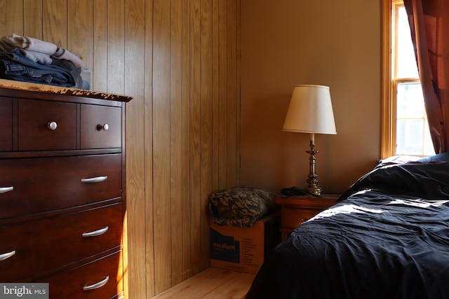 bedroom with multiple windows, wood-type flooring, and wooden walls