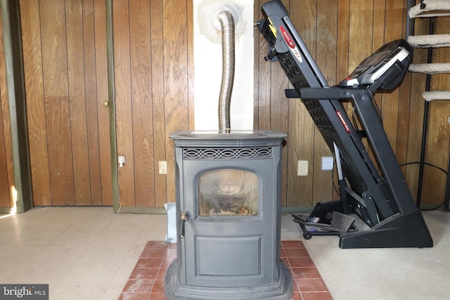 exercise room with wood walls, light tile patterned floors, and a wood stove