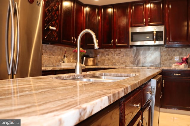 kitchen with light stone counters, stainless steel appliances, sink, and decorative backsplash