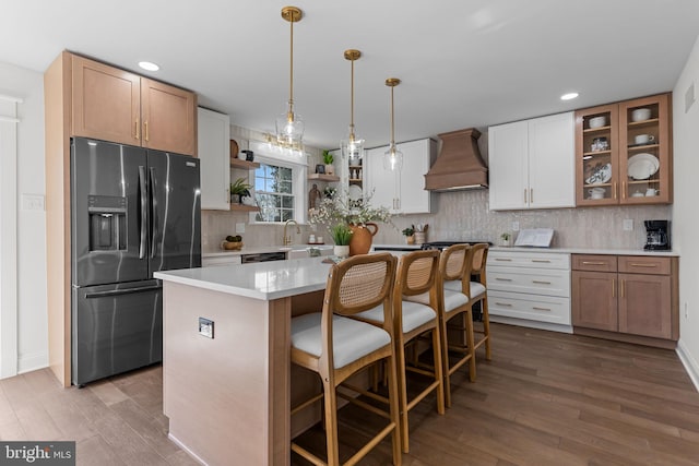 kitchen with black refrigerator with ice dispenser, a center island, white cabinets, and premium range hood