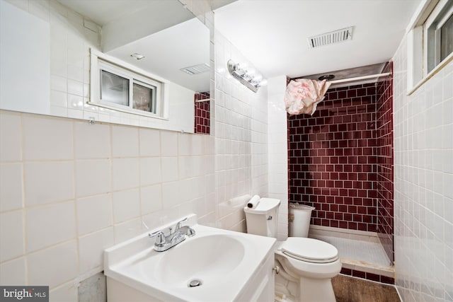 bathroom featuring vanity, tiled shower, tile walls, and toilet