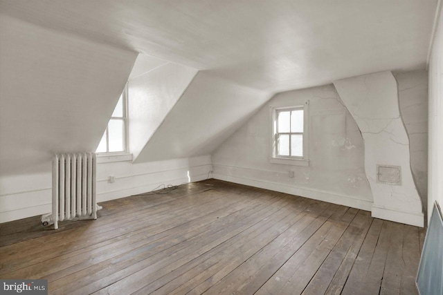 bonus room with wood-type flooring, vaulted ceiling, and radiator