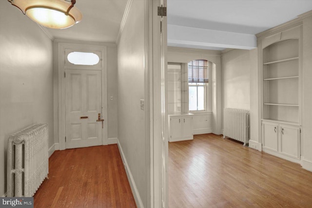 foyer entrance with hardwood / wood-style flooring, ornamental molding, and radiator heating unit