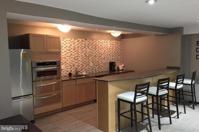 kitchen featuring sink, stainless steel appliances, a kitchen bar, decorative backsplash, and kitchen peninsula