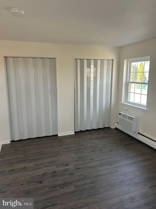 unfurnished bedroom with multiple closets, dark wood-type flooring, and a wall mounted air conditioner