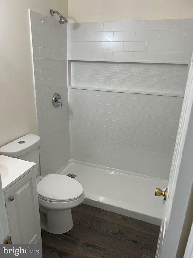 bathroom featuring vanity, hardwood / wood-style flooring, toilet, and a tile shower