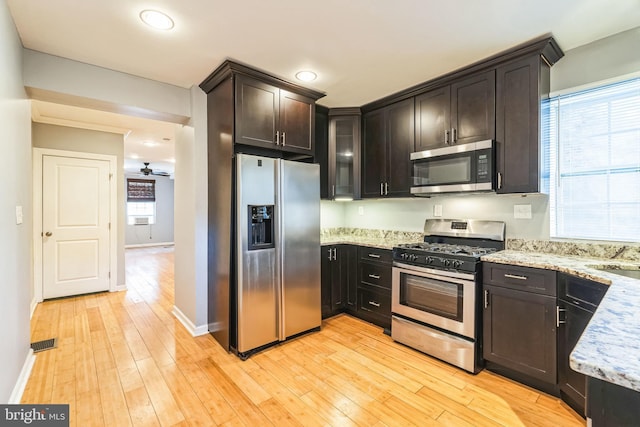 kitchen featuring dark brown cabinetry, light stone countertops, light hardwood / wood-style floors, and appliances with stainless steel finishes