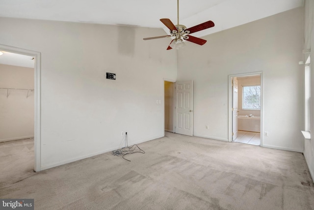 unfurnished bedroom featuring a walk in closet, ensuite bath, carpet, baseboards, and a towering ceiling