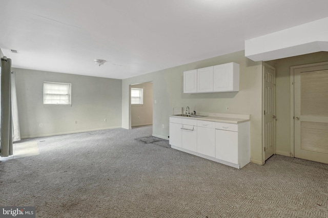 kitchen featuring baseboards, light countertops, light carpet, white cabinetry, and a sink