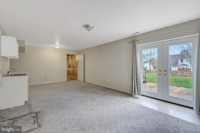 unfurnished living room featuring visible vents, light carpet, a sink, french doors, and baseboards