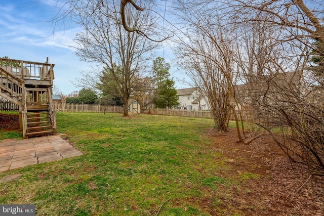 view of yard featuring an outbuilding, a deck, a fenced backyard, a shed, and stairs