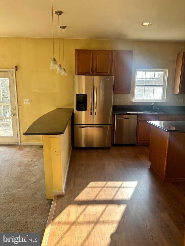 kitchen with a peninsula, dark countertops, appliances with stainless steel finishes, and a sink