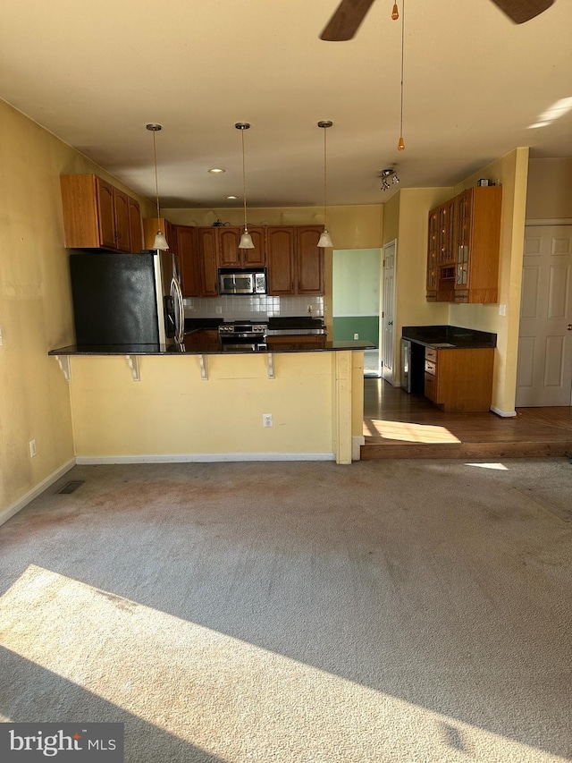 kitchen with dark countertops, backsplash, decorative light fixtures, appliances with stainless steel finishes, and a ceiling fan