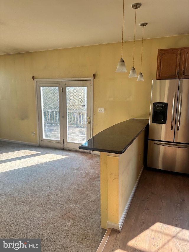 kitchen with a peninsula, stainless steel refrigerator with ice dispenser, dark countertops, decorative light fixtures, and dark carpet