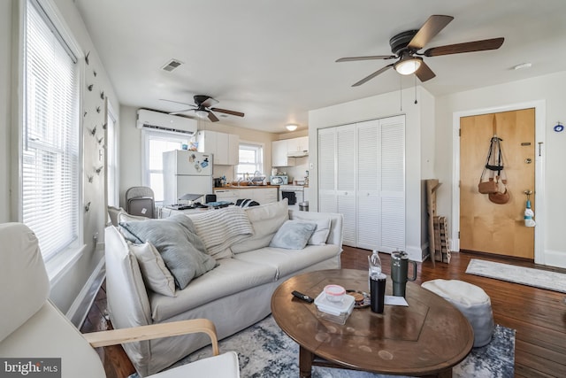 living room featuring ceiling fan, dark hardwood / wood-style floors, and a wall unit AC