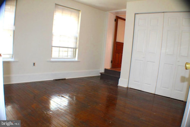 unfurnished bedroom featuring multiple windows, dark wood-type flooring, and a closet