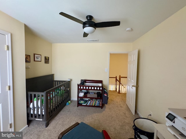 bedroom with light carpet, a nursery area, and ceiling fan