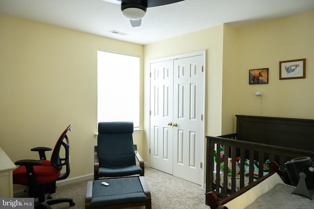 bedroom featuring a nursery area, light carpet, ceiling fan, and a closet