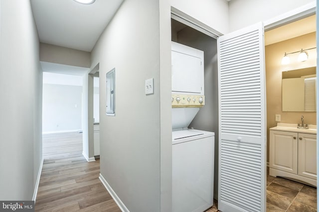 laundry room with stacked washer / drying machine, sink, electric panel, and light hardwood / wood-style floors