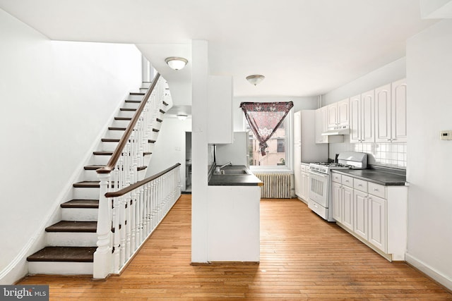 kitchen with sink, white cabinetry, radiator heating unit, white gas stove, and light wood-type flooring