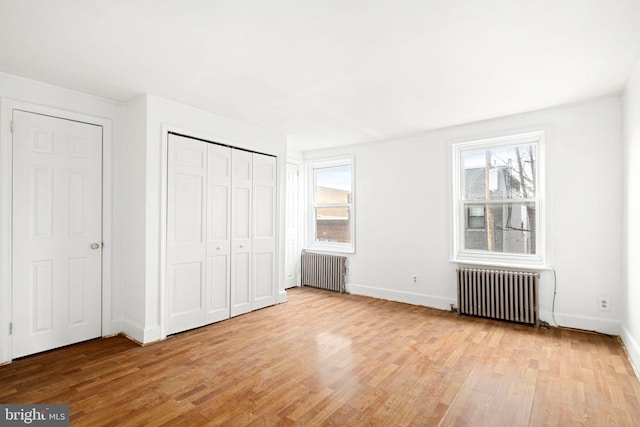 unfurnished bedroom featuring multiple windows, radiator heating unit, and light wood-type flooring